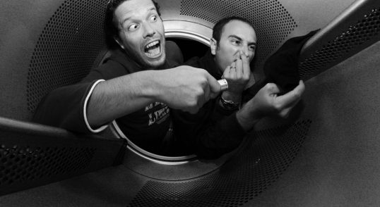 Două persoane într-un spațiu restrâns, una arătând o expresie de surpriză, iar cealaltă acoperindu-și nasul.