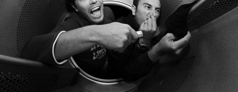 Două persoane într-un spațiu restrâns, una arătând o expresie de surpriză, iar cealaltă acoperindu-și nasul.