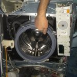 Interiorul unei mașini de spălat cu un bărbat care arată un component.