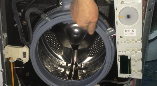 Interiorul unei mașini de spălat cu un bărbat care arată un component.