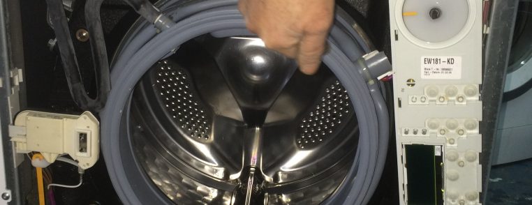 Interiorul unei mașini de spălat cu un bărbat care arată un component.